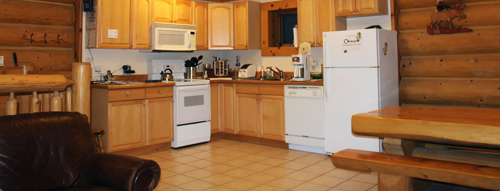 A cozy log cabin kitchen featuring wooden cabinets, white appliances, and a dining table.
